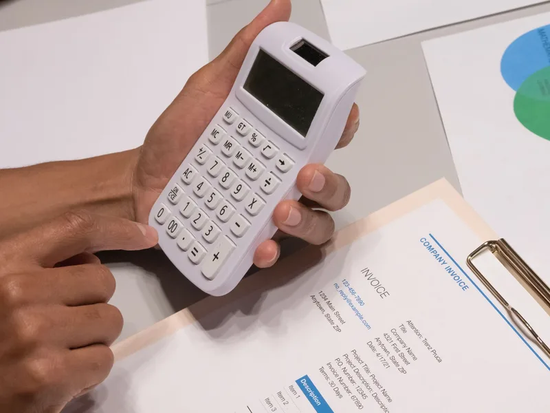 Close-up of hands using a calculator next to an invoice, representing rate-setting and invoicing for freelance VA work