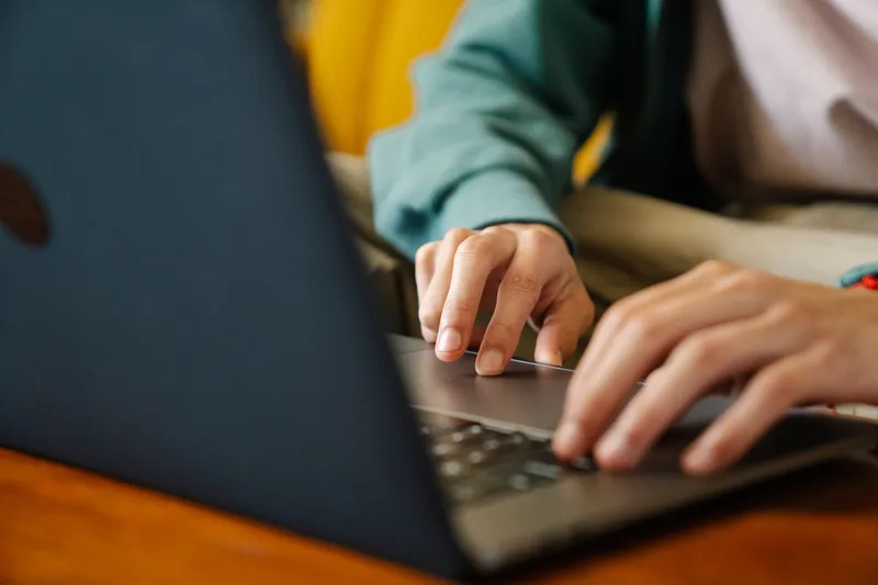 Close-up of hands typing on a laptop while building a virtual assistant portfolio and profile