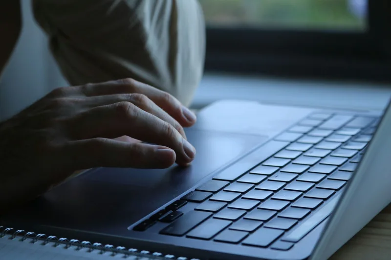 Close-up of hands typing on a laptop keyboard next to a notebook, representing non-voice VA task work like product listing and order processing