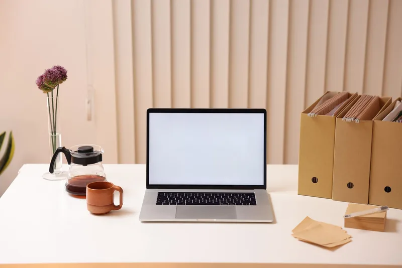 A laptop, coffee, and organized file folders on a clean desk