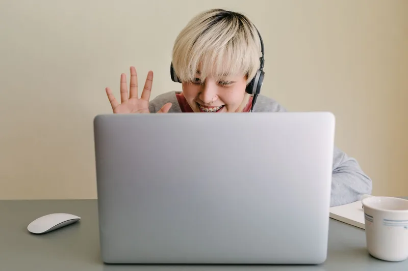 Woman smiling and waving during a video call on a laptop