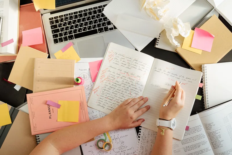 Overhead shot of a person organizing notes and study materials with a laptop, representing self-directed practice for a new ecommerce VA