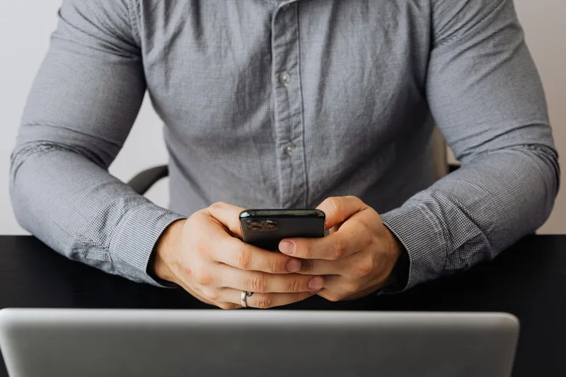 Person checking a smartphone next to a laptop, representing the chat and communication tools an ecommerce VA uses daily