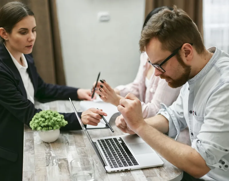 Three professionals collaborating around a laptop, representing an agency support and training team