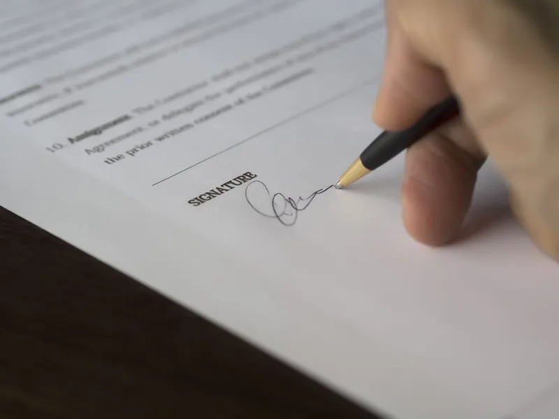 A hand signing a formal work agreement or contract on a desk