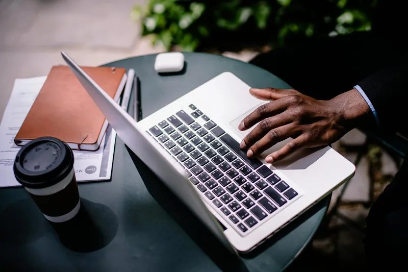 Person working on a laptop at a cafe table with documents and coffee, browsing job listings
