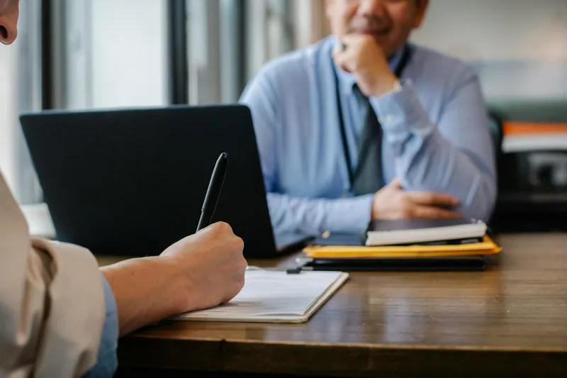Person completing a job application form at a desk with documents and a laptop nearby