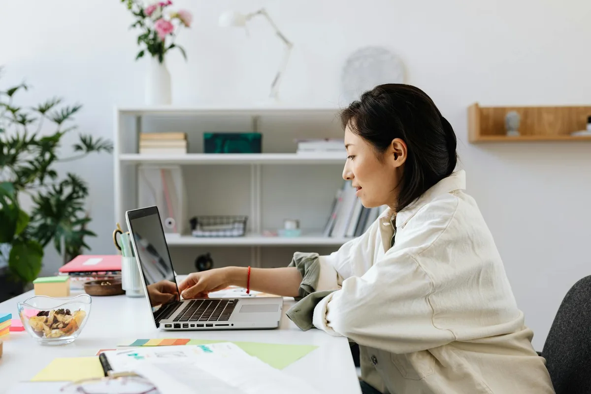 Filipino virtual assistant reviewing salary benchmarks on a laptop at a home desk with peso signs visible