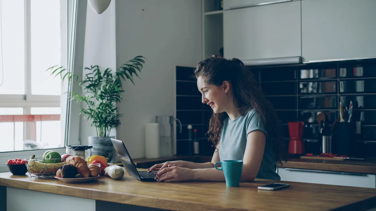 Filipino virtual assistant working on laptop in bright kitchen setting